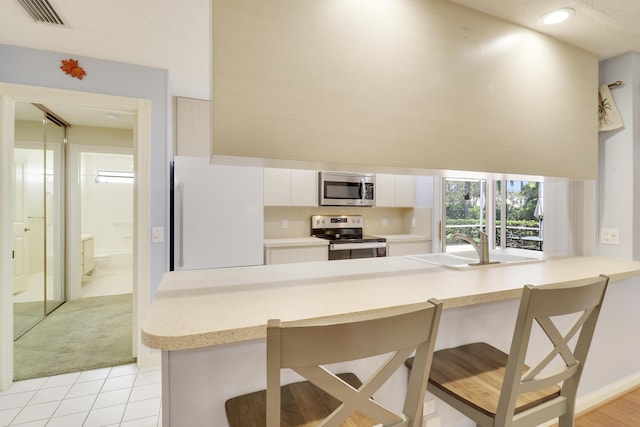 kitchen with a kitchen bar, light tile patterned floors, kitchen peninsula, stainless steel appliances, and white cabinets