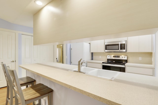 kitchen featuring appliances with stainless steel finishes, sink, white cabinets, and a breakfast bar