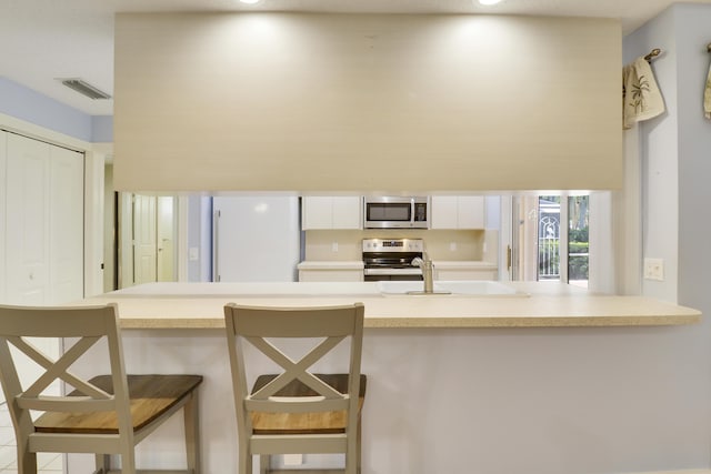 kitchen with appliances with stainless steel finishes, a breakfast bar, and white cabinets