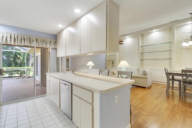 kitchen with sink, white cabinetry, hanging light fixtures, stainless steel dishwasher, and kitchen peninsula