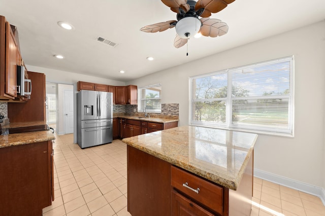 kitchen featuring backsplash, light tile patterned flooring, light stone countertops, and appliances with stainless steel finishes