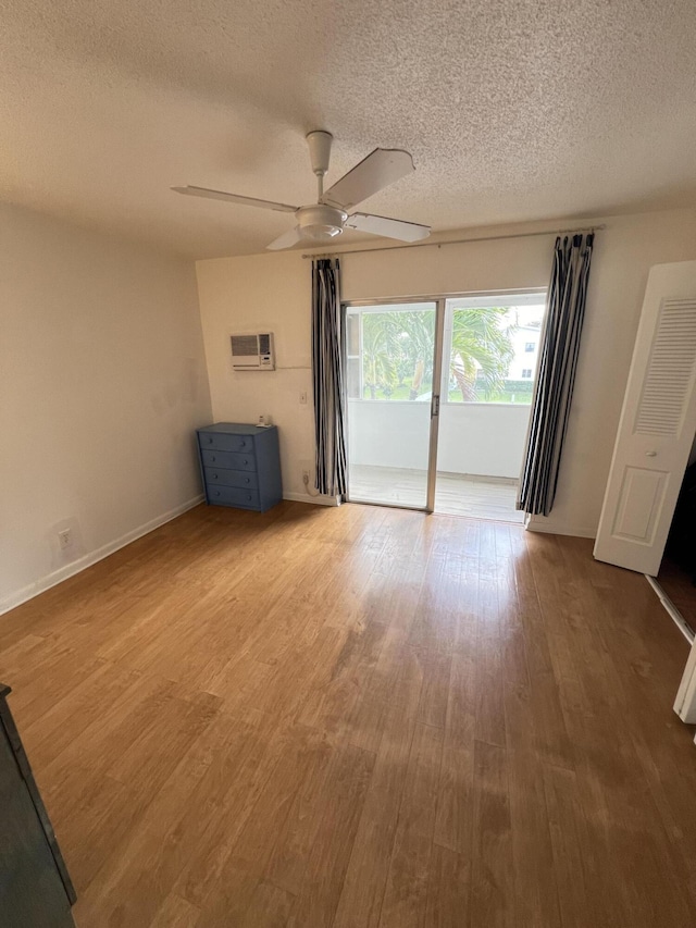 empty room with a wall mounted air conditioner, a textured ceiling, wood-type flooring, and ceiling fan