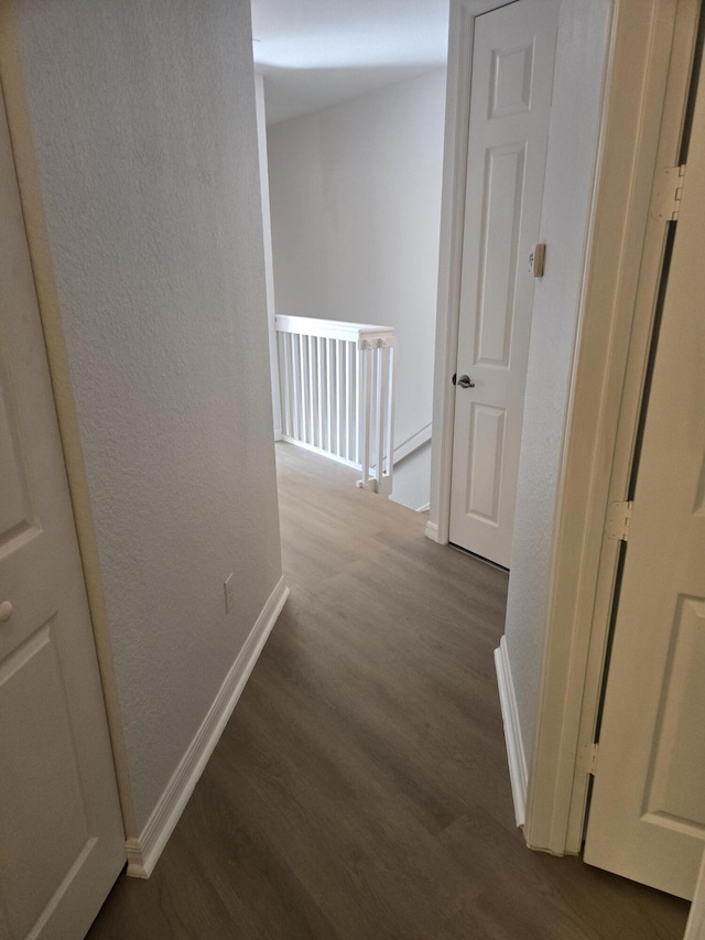 corridor featuring an upstairs landing, a textured wall, baseboards, and wood finished floors