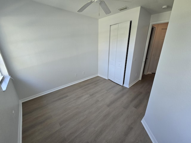 unfurnished bedroom featuring ceiling fan, dark wood-type flooring, visible vents, baseboards, and a closet