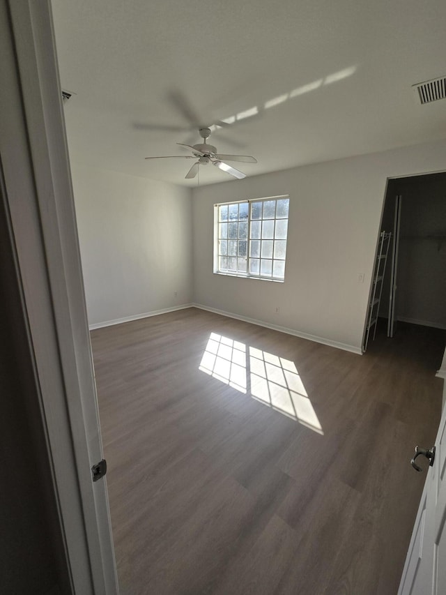 unfurnished room with baseboards, visible vents, dark wood finished floors, and a ceiling fan