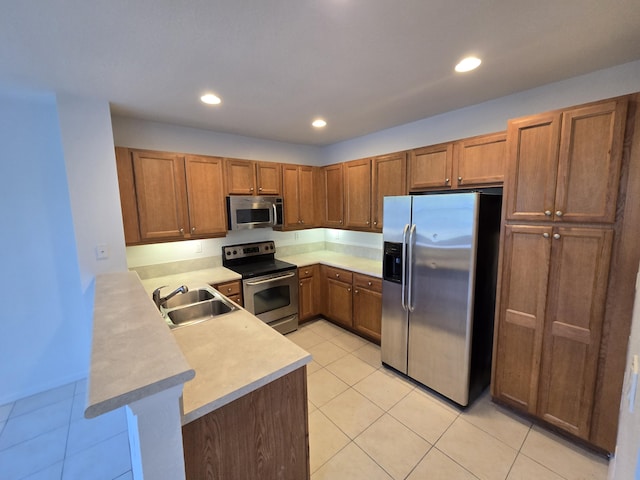 kitchen with stainless steel appliances, a peninsula, a sink, light countertops, and brown cabinets