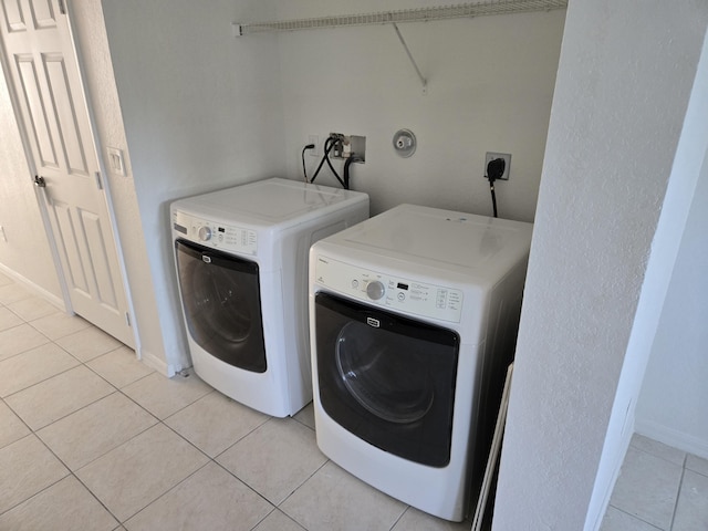 washroom with laundry area, light tile patterned floors, baseboards, and washing machine and clothes dryer