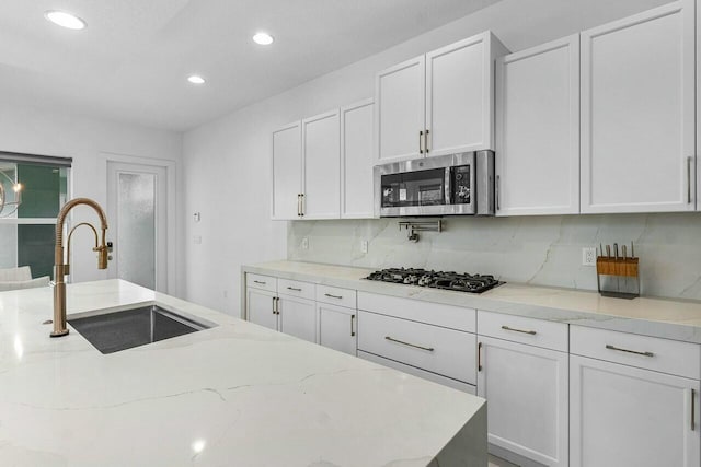 kitchen featuring white cabinetry, black gas cooktop, light stone countertops, and sink