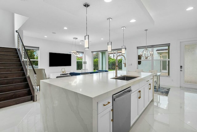 kitchen featuring sink, white cabinets, stainless steel dishwasher, light stone countertops, and a center island with sink