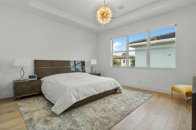 bedroom featuring a notable chandelier, a tray ceiling, and light hardwood / wood-style floors