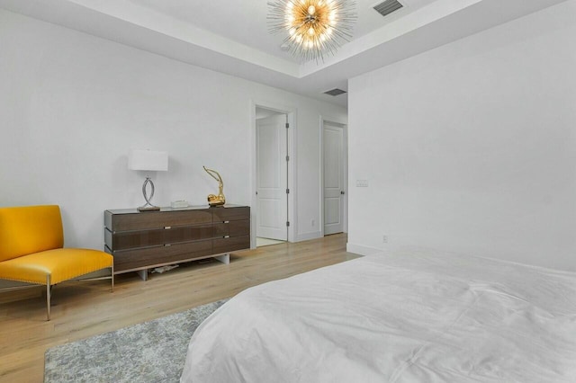 bedroom featuring a raised ceiling, a chandelier, and light wood-type flooring