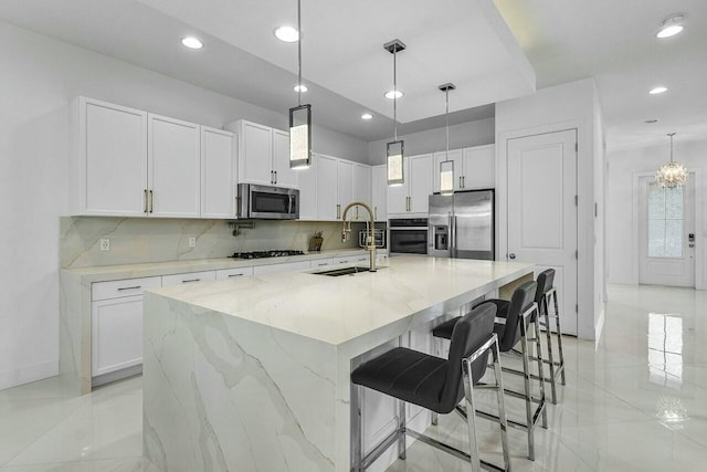 kitchen with sink, stainless steel appliances, a spacious island, light stone counters, and white cabinets