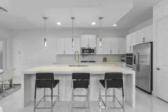 kitchen with stainless steel appliances, white cabinetry, hanging light fixtures, and an island with sink