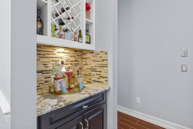 bar with light stone countertops, backsplash, and dark hardwood / wood-style flooring