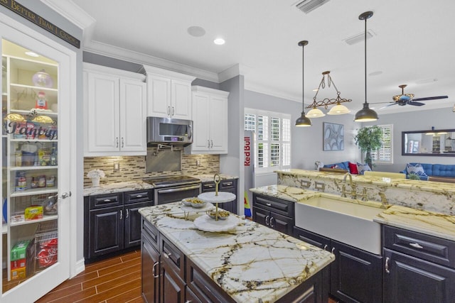 kitchen featuring sink, stainless steel appliances, white cabinets, a kitchen island, and decorative light fixtures