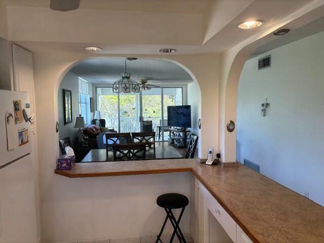 kitchen featuring white refrigerator, hanging light fixtures, a breakfast bar area, and kitchen peninsula