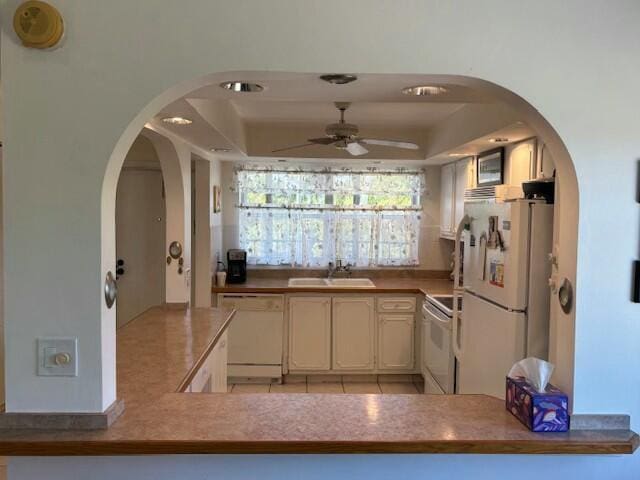 kitchen with sink, white appliances, a raised ceiling, kitchen peninsula, and ceiling fan