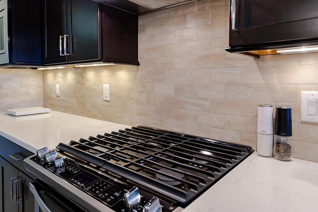 kitchen with stainless steel gas range, light stone counters, and tasteful backsplash