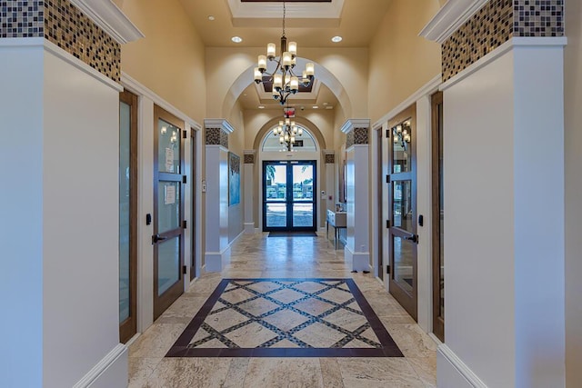 entrance foyer with french doors, a towering ceiling, an inviting chandelier, a tray ceiling, and ornamental molding