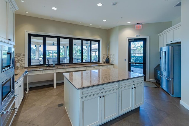 kitchen featuring backsplash, stainless steel appliances, white cabinets, and light stone counters