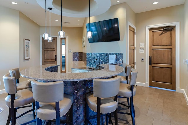 kitchen featuring light stone countertops, pendant lighting, sink, a kitchen bar, and kitchen peninsula