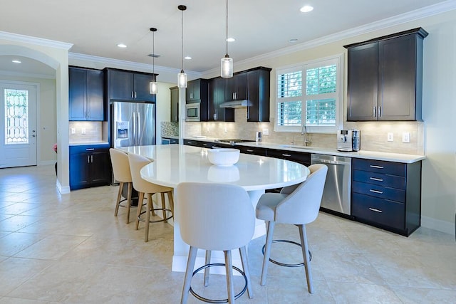 kitchen with hanging light fixtures, stainless steel appliances, a kitchen island, a breakfast bar, and ornamental molding