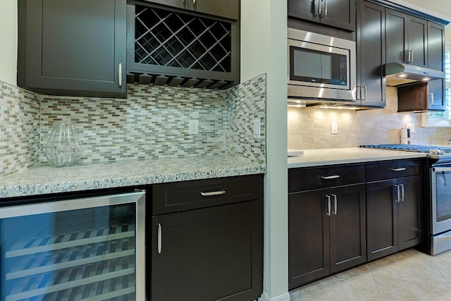 kitchen featuring wine cooler, tasteful backsplash, light stone counters, light tile patterned floors, and appliances with stainless steel finishes