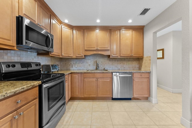 kitchen featuring sink, light tile patterned floors, appliances with stainless steel finishes, tasteful backsplash, and light stone countertops