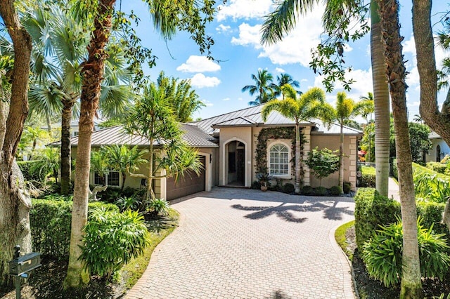 mediterranean / spanish-style house featuring decorative driveway, stucco siding, a standing seam roof, metal roof, and a garage