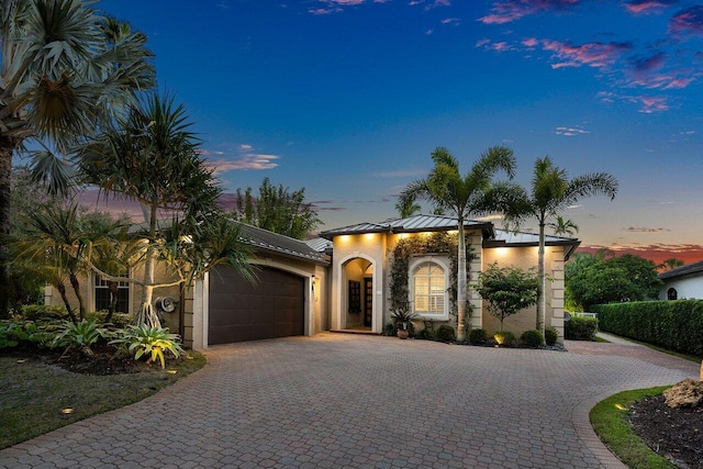 mediterranean / spanish-style home with a garage, metal roof, a standing seam roof, decorative driveway, and stucco siding