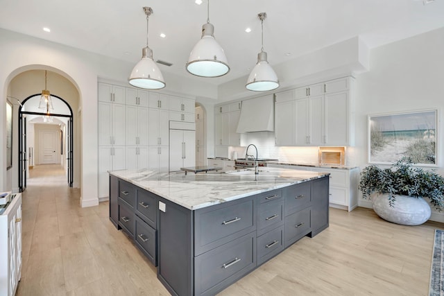 kitchen with decorative light fixtures, white cabinets, paneled built in fridge, custom range hood, and a spacious island