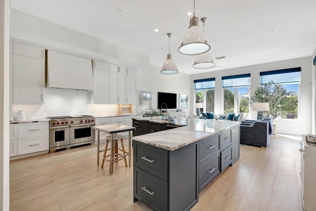 kitchen featuring a kitchen island with sink, double oven range, white cabinetry, and pendant lighting