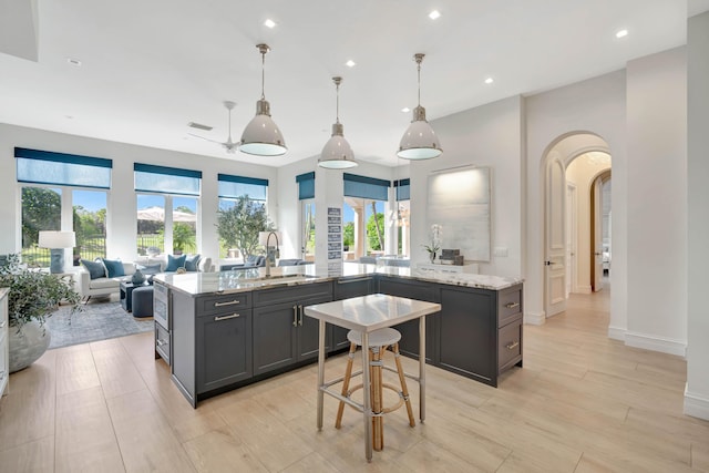 kitchen with sink, a spacious island, light stone counters, light hardwood / wood-style floors, and decorative light fixtures