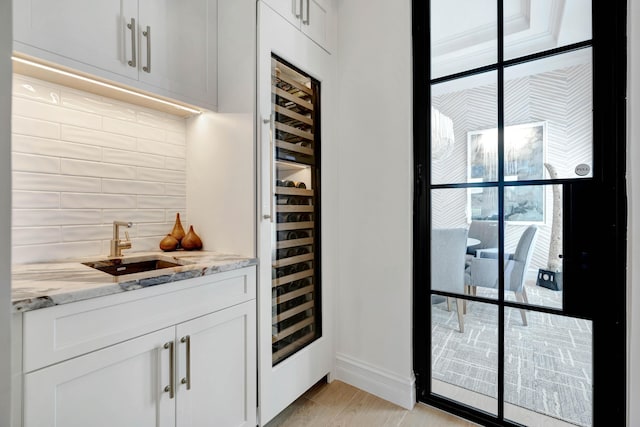 bar featuring white cabinetry, light stone counters, beverage cooler, and decorative backsplash