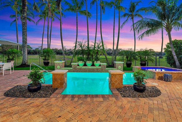 pool at dusk with an in ground hot tub and a patio area