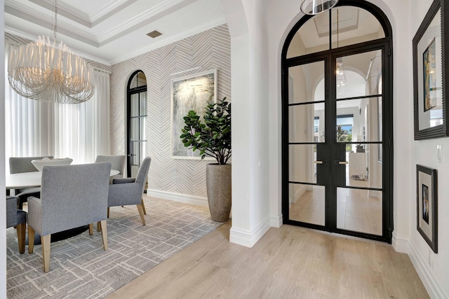 dining space with french doors, a chandelier, light hardwood / wood-style flooring, ornamental molding, and a raised ceiling