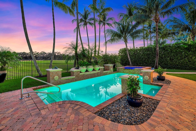 pool at dusk with an in ground hot tub, a yard, and a patio area