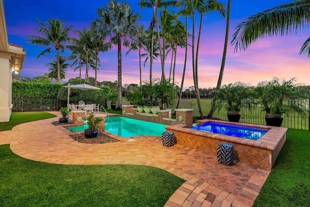 pool at dusk featuring a jacuzzi, a lawn, and a patio