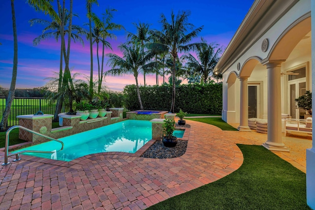 pool at dusk featuring a patio and an in ground hot tub