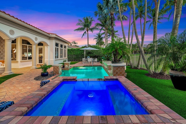 pool at dusk featuring a patio area, a lawn, and an in ground hot tub