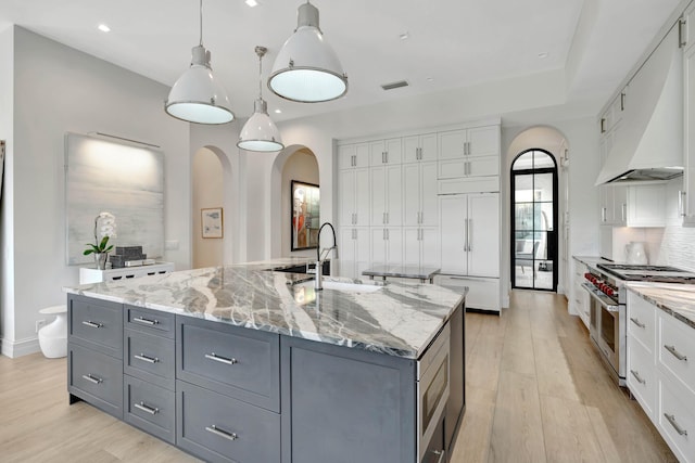 kitchen with pendant lighting, premium range hood, a kitchen island with sink, white cabinetry, and high end appliances