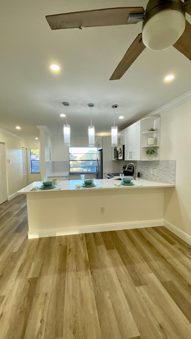 kitchen with light countertops, appliances with stainless steel finishes, pendant lighting, white cabinetry, and a peninsula