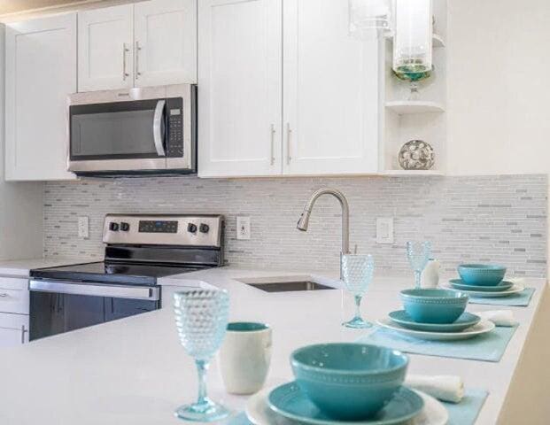 kitchen with a sink, light countertops, white cabinets, stainless steel appliances, and open shelves