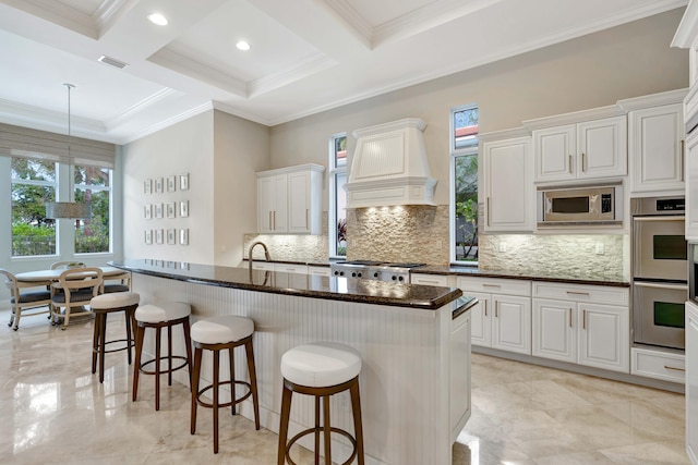 kitchen featuring custom exhaust hood, a center island with sink, appliances with stainless steel finishes, a kitchen breakfast bar, and white cabinets