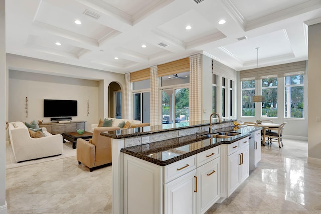 kitchen with decorative light fixtures, sink, white cabinets, dark stone counters, and a center island with sink