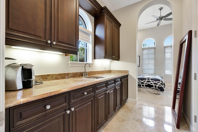 kitchen with sink, ceiling fan, dark brown cabinets, ornamental molding, and light stone countertops