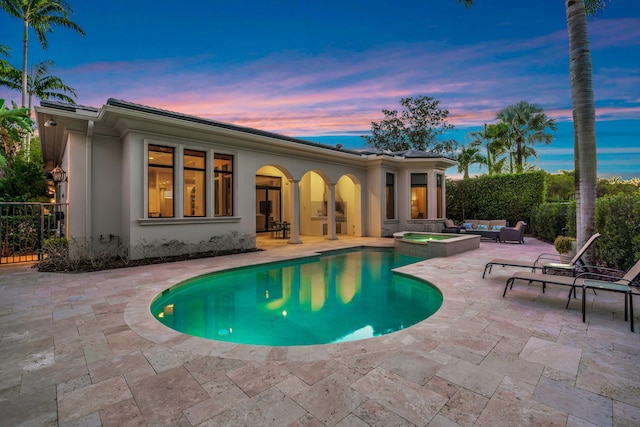 pool at dusk with an in ground hot tub, an outdoor hangout area, and a patio