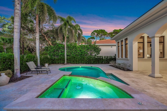 pool at dusk featuring a patio and an in ground hot tub