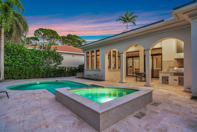 pool at dusk with exterior kitchen, an in ground hot tub, area for grilling, and a patio