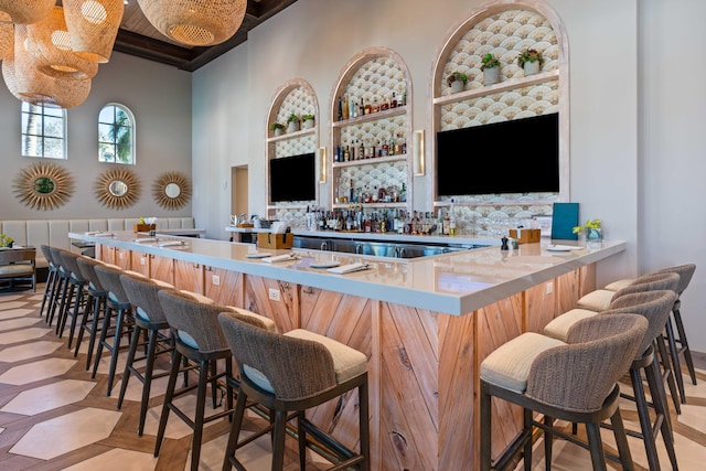 bar with built in shelves, beam ceiling, and a high ceiling